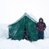 Girl standing next to tent in snow